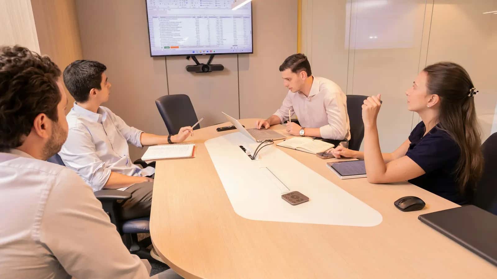 Réunion de direction autour d'une table de conférence, avec un écran affichant des tableaux