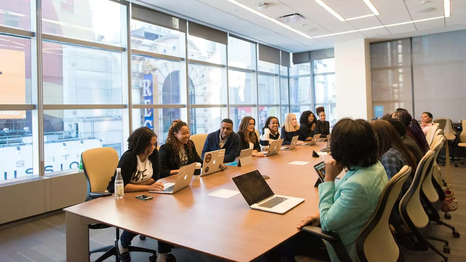 Adultes en formation avec leurs ordinateurs portables autour d'une grande table de réunion