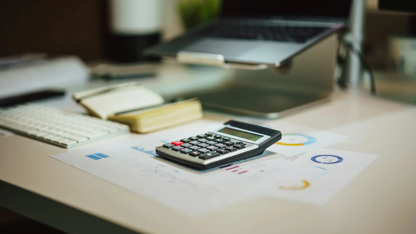 Calculatrice posée sur des documents chiffrés à côté d'un ordinateur portable sur un bureau