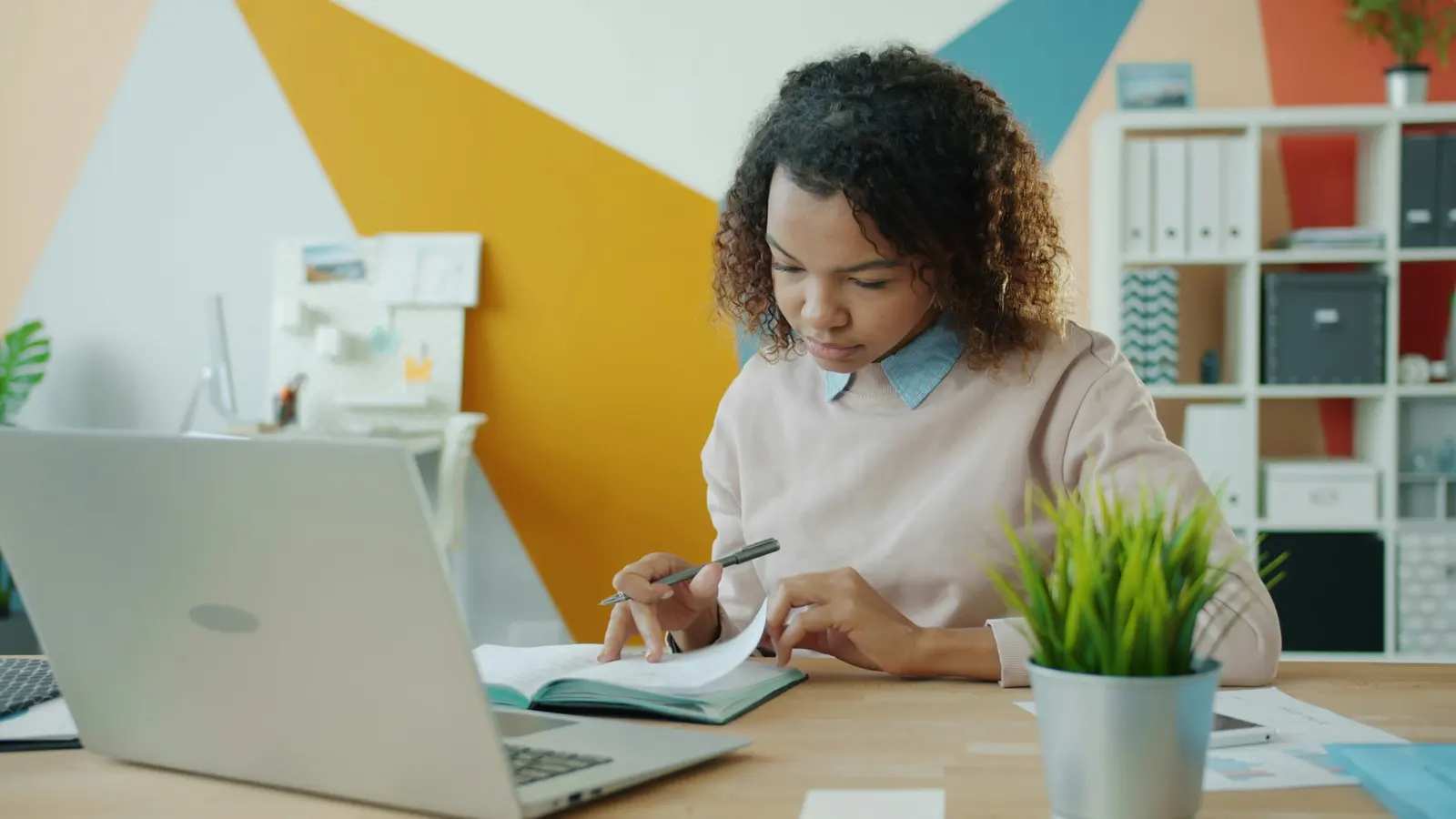 Jeune femme prenant des notes dans un cahier devant son ordinateur portable, au bureau