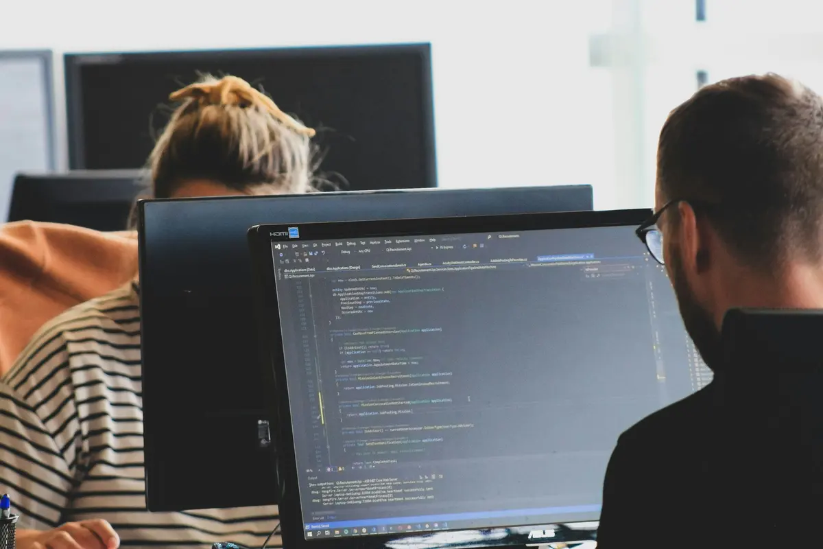 Deux professionnels travaillant sur des écrans affichant du code dans un open space