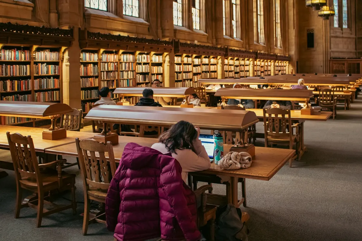 Students working on laptops in a large university library reading room