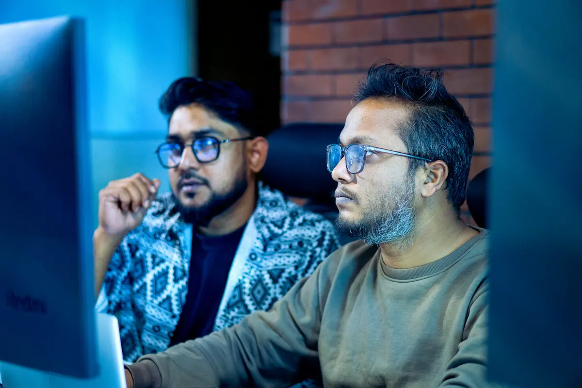 Two IT professionals in glasses working together in front of a monitor