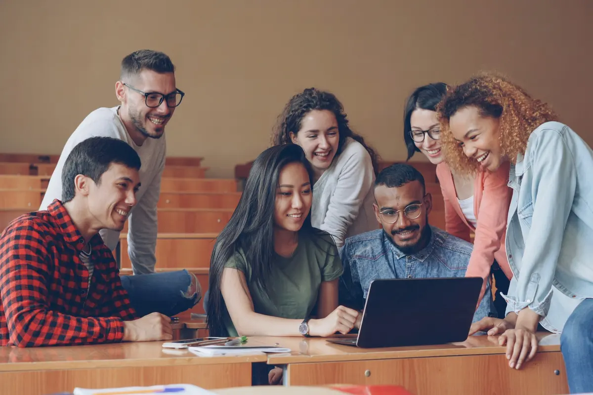 Groupe d'étudiants souriants réunis autour d'un ordinateur portable dans un amphithéâtre