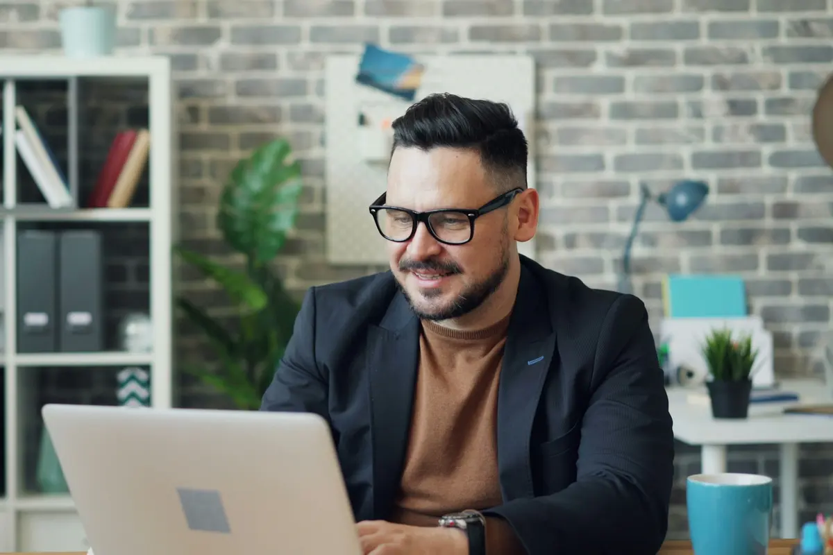 Smiling man in a blazer working on his laptop in an office